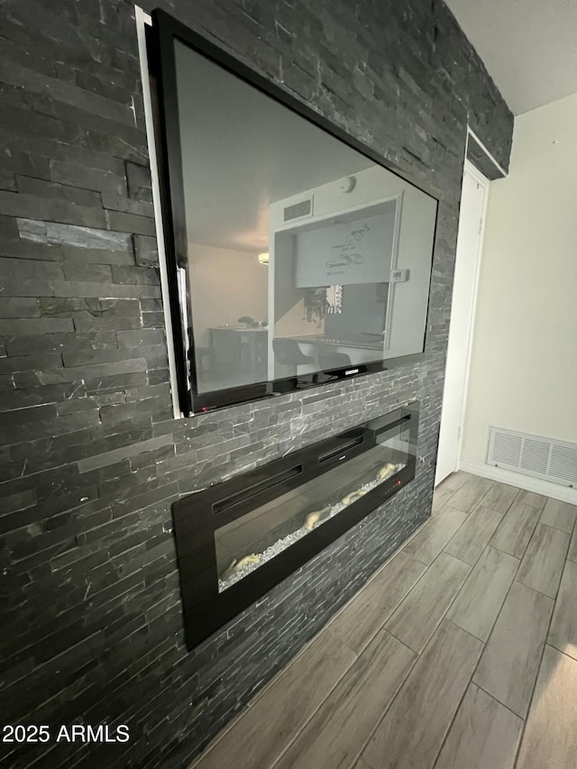 detailed view of a glass covered fireplace, wood tiled floors, and baseboards