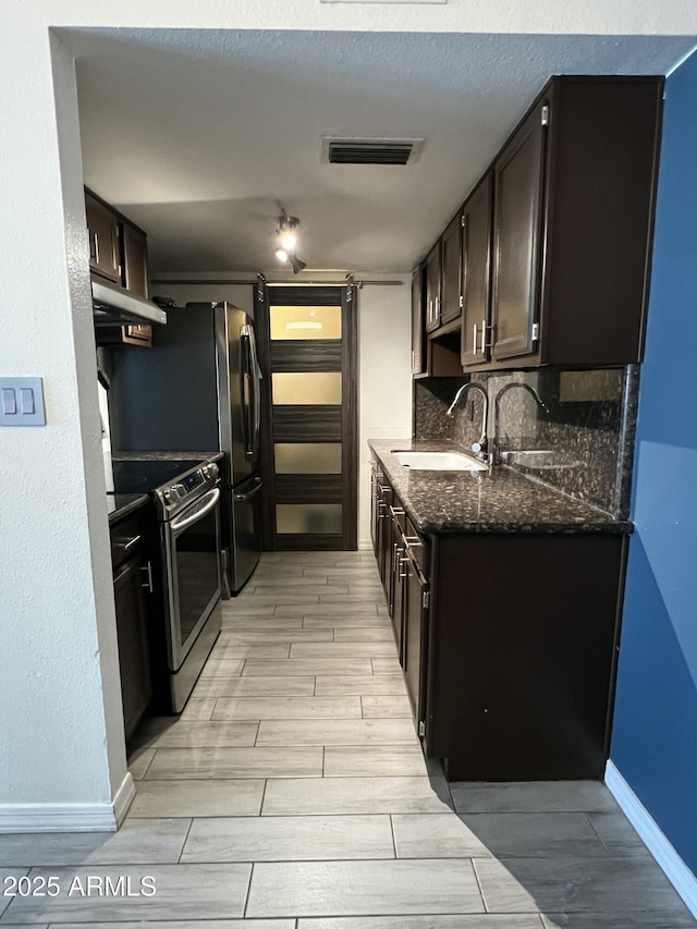 kitchen with stainless steel range with electric cooktop, a sink, wood tiled floors, dark stone counters, and dark brown cabinetry