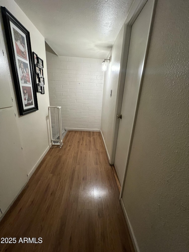 corridor with wood finished floors, baseboards, a textured ceiling, and an upstairs landing