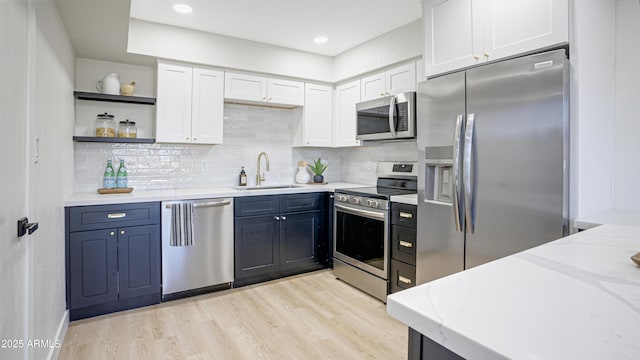 kitchen with light stone countertops, appliances with stainless steel finishes, blue cabinets, sink, and white cabinetry