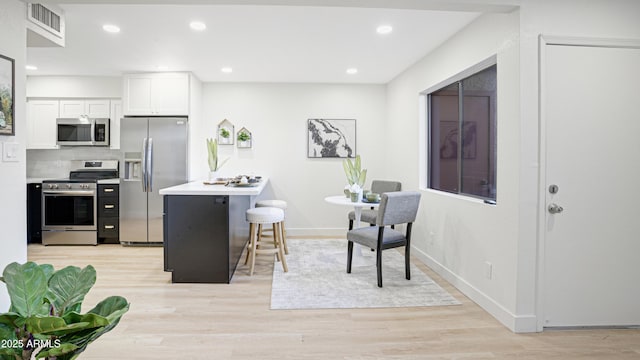 kitchen with white cabinets, a breakfast bar, light wood-type flooring, and appliances with stainless steel finishes