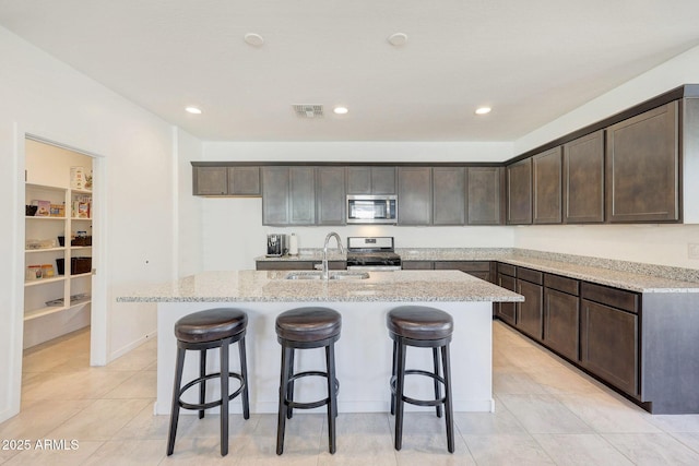 kitchen featuring appliances with stainless steel finishes, a kitchen island with sink, sink, and light stone countertops