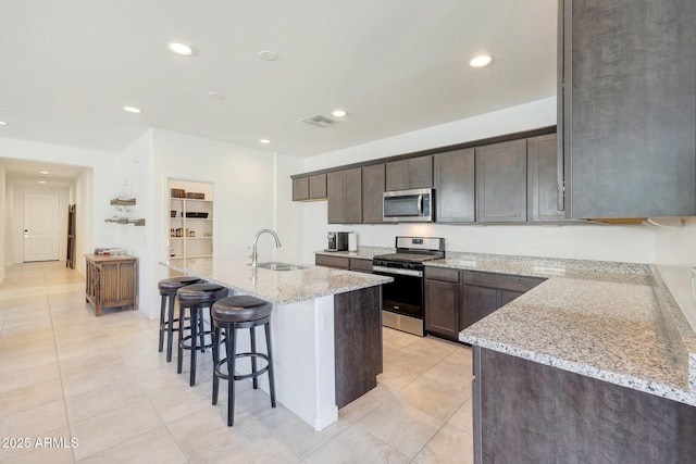 kitchen with light tile patterned flooring, sink, a kitchen island with sink, light stone counters, and stainless steel appliances