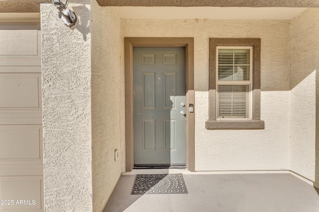 view of exterior entry with a garage and stucco siding