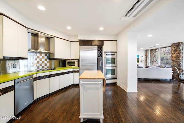 kitchen with white cabinets, wall chimney exhaust hood, stainless steel appliances, and dark wood finished floors