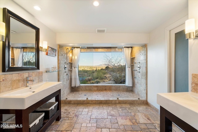 bathroom featuring visible vents, a tile shower, stone tile flooring, and vanity