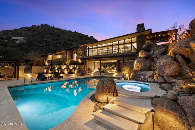 pool at dusk with a patio area, an outdoor pool, and an in ground hot tub