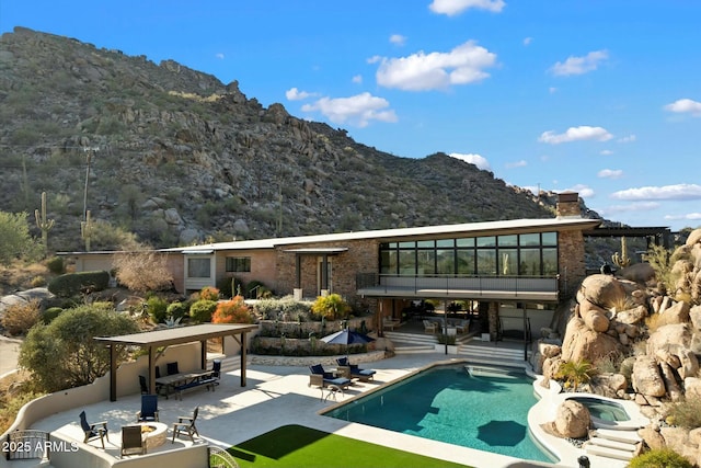 back of house featuring an in ground hot tub, a chimney, a patio area, and a mountain view