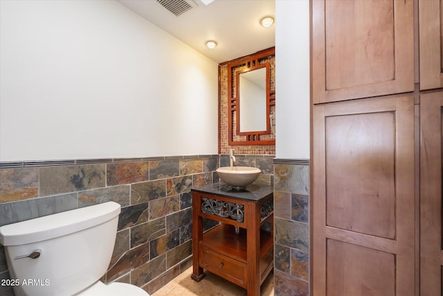 bathroom with vanity, toilet, and tile walls