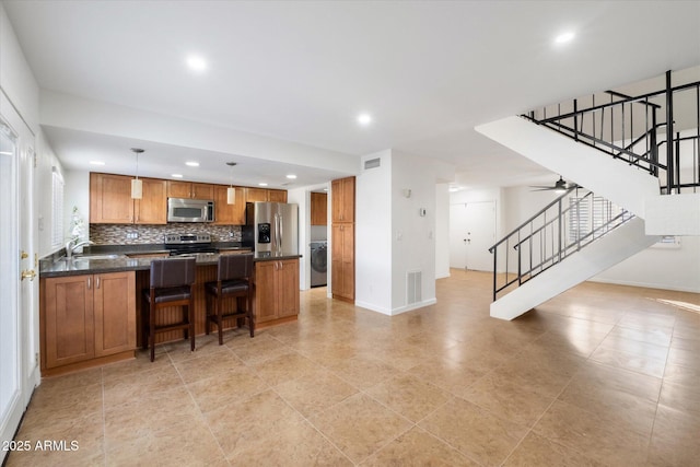 kitchen with a breakfast bar area, tasteful backsplash, appliances with stainless steel finishes, pendant lighting, and washer / clothes dryer