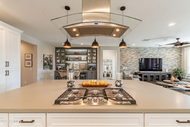 kitchen featuring stainless steel gas cooktop, white cabinetry, hanging light fixtures, ceiling fan, and island exhaust hood