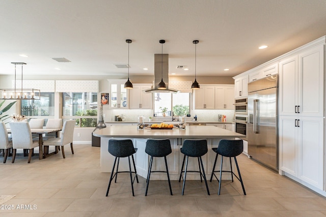 kitchen with an island with sink, white cabinets, island exhaust hood, decorative light fixtures, and built in fridge