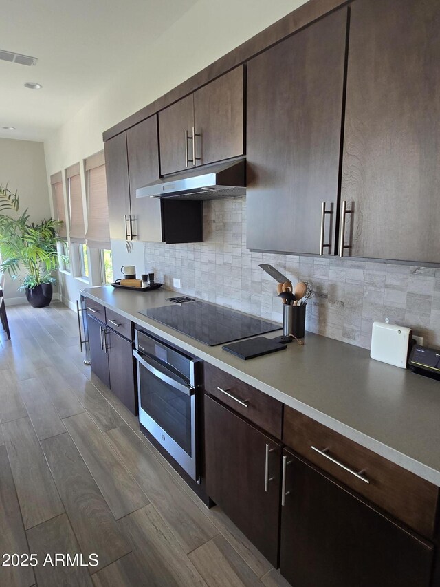 17833 E Veit Springs Dr, Rio Verde, AZ 85263 - kitchen featuring decorative backsplash, black electric cooktop, dark brown cabinets, under cabinet range hood, and oven