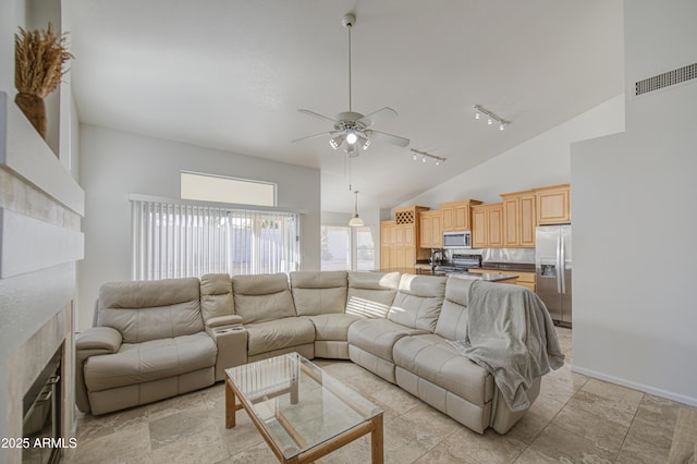 living room featuring ceiling fan, rail lighting, high vaulted ceiling, a tiled fireplace, and visible vents
