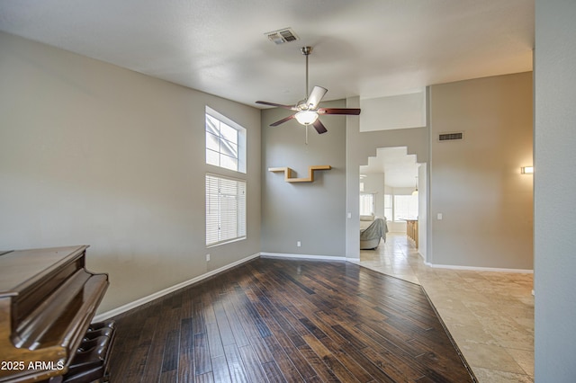 interior space featuring a ceiling fan, baseboards, visible vents, and a towering ceiling
