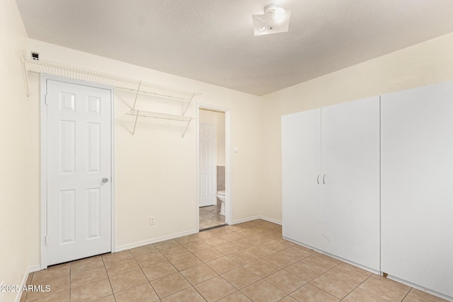 unfurnished bedroom with light tile patterned floors, ensuite bath, and a textured ceiling