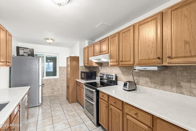 kitchen with light stone counters, light tile patterned floors, stainless steel appliances, and tile walls