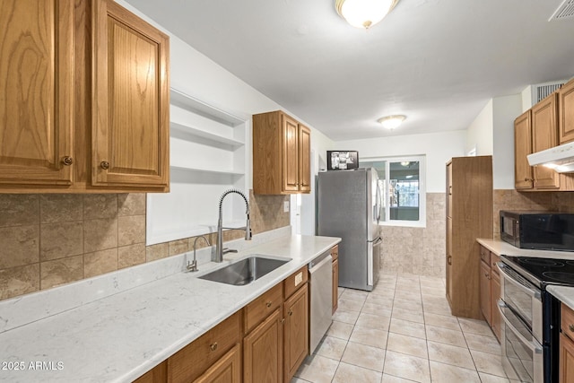 kitchen with sink, tile walls, light tile patterned floors, stainless steel appliances, and light stone countertops