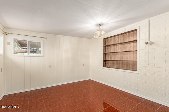 spare room with an inviting chandelier and brick wall