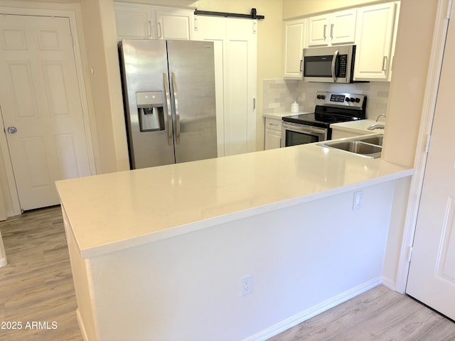 kitchen with kitchen peninsula, appliances with stainless steel finishes, a barn door, and white cabinets