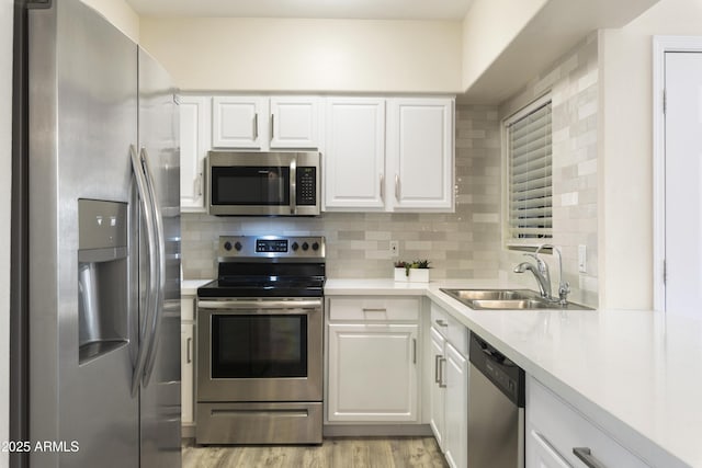 kitchen featuring white cabinetry, sink, decorative backsplash, appliances with stainless steel finishes, and light wood-type flooring