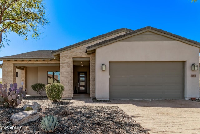 view of front of home featuring a tiled roof, stucco siding, an attached garage, and decorative driveway