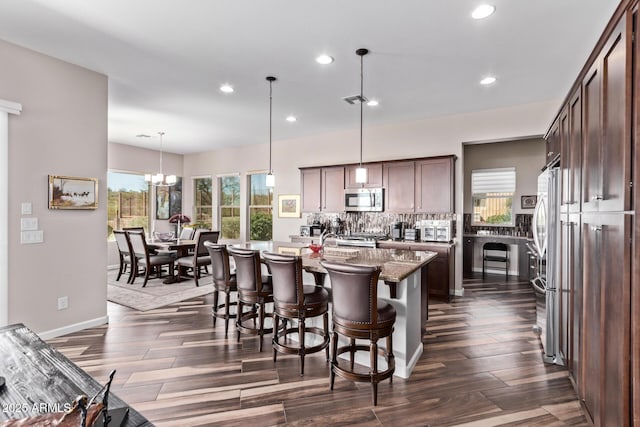 kitchen featuring stainless steel appliances, backsplash, dark brown cabinets, and dark wood-style flooring