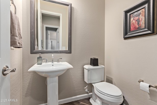 bathroom with a textured wall, toilet, baseboards, and wood finished floors