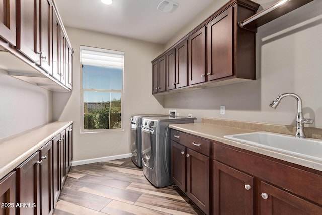 washroom featuring light wood-style flooring, a sink, cabinet space, baseboards, and washing machine and clothes dryer