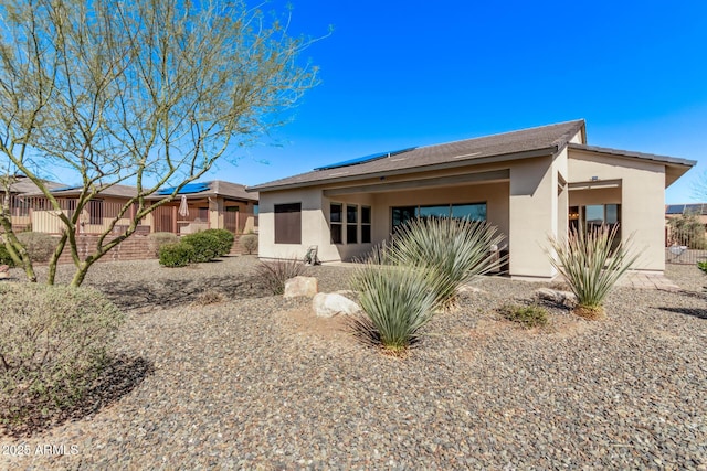 view of front of house featuring stucco siding, solar panels, and fence