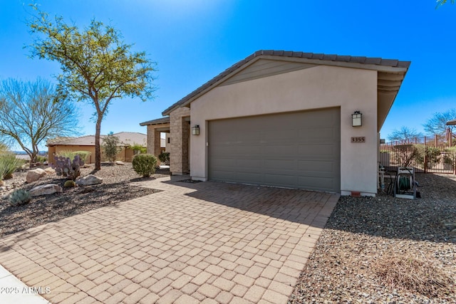 view of front of property with stucco siding, decorative driveway, a garage, and fence