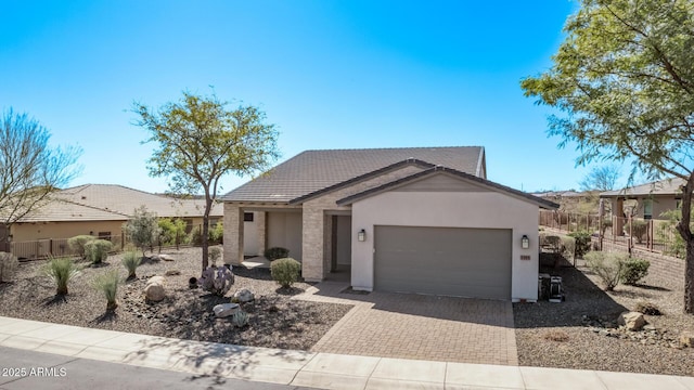 view of front facade featuring fence, stucco siding, a garage, a tile roof, and decorative driveway