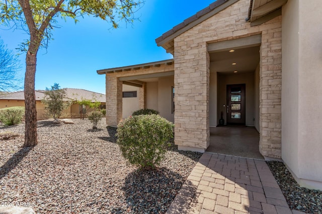 property entrance with fence, stone siding, and stucco siding