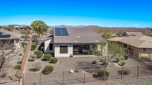 rear view of property with fence, roof mounted solar panels, stucco siding, a mountain view, and a patio