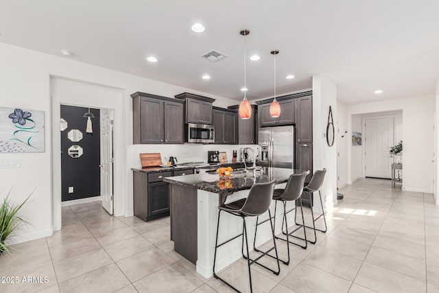 kitchen featuring sink, appliances with stainless steel finishes, hanging light fixtures, dark brown cabinets, and a center island with sink