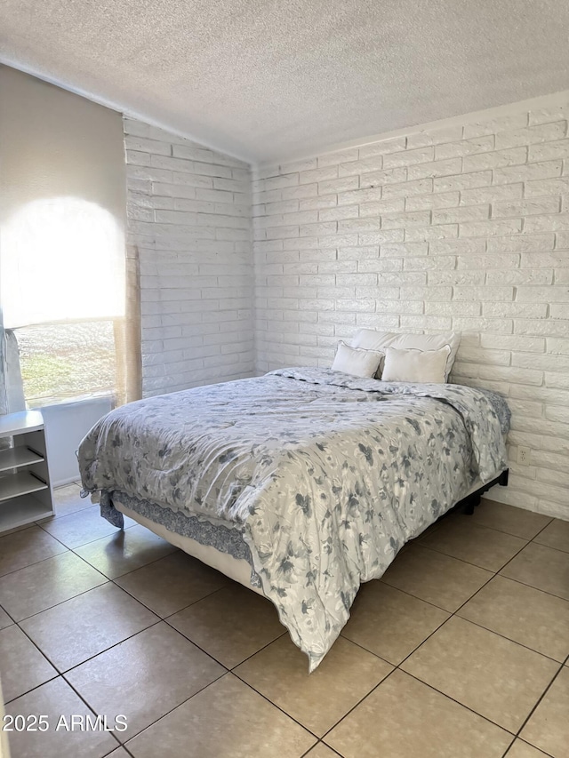 bedroom with light tile patterned floors, brick wall, a textured ceiling, and vaulted ceiling