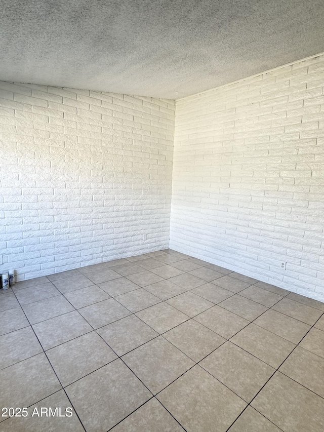 tiled empty room featuring brick wall and a textured ceiling