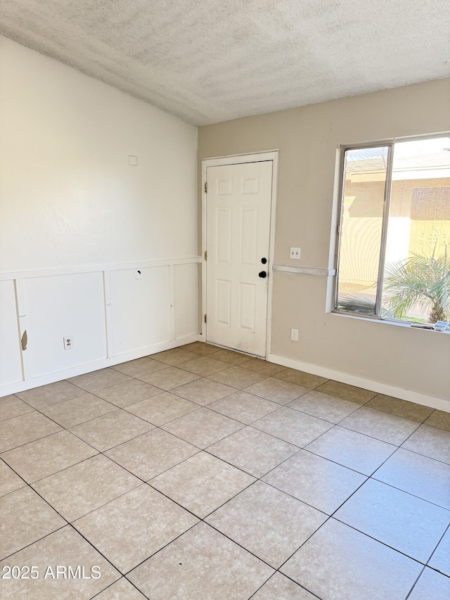 unfurnished room with a decorative wall, light tile patterned floors, wainscoting, and a textured ceiling