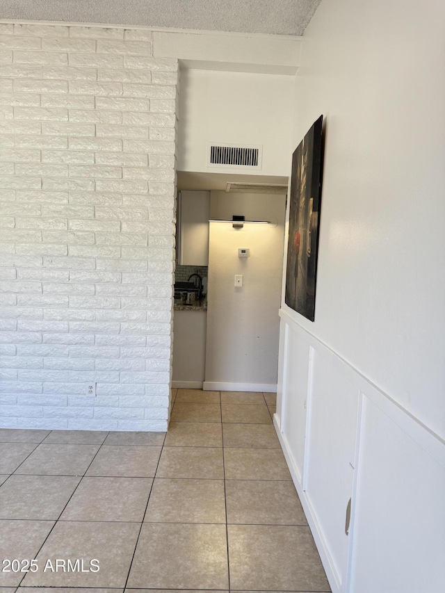 hallway featuring tile patterned flooring, visible vents, brick wall, and a textured ceiling