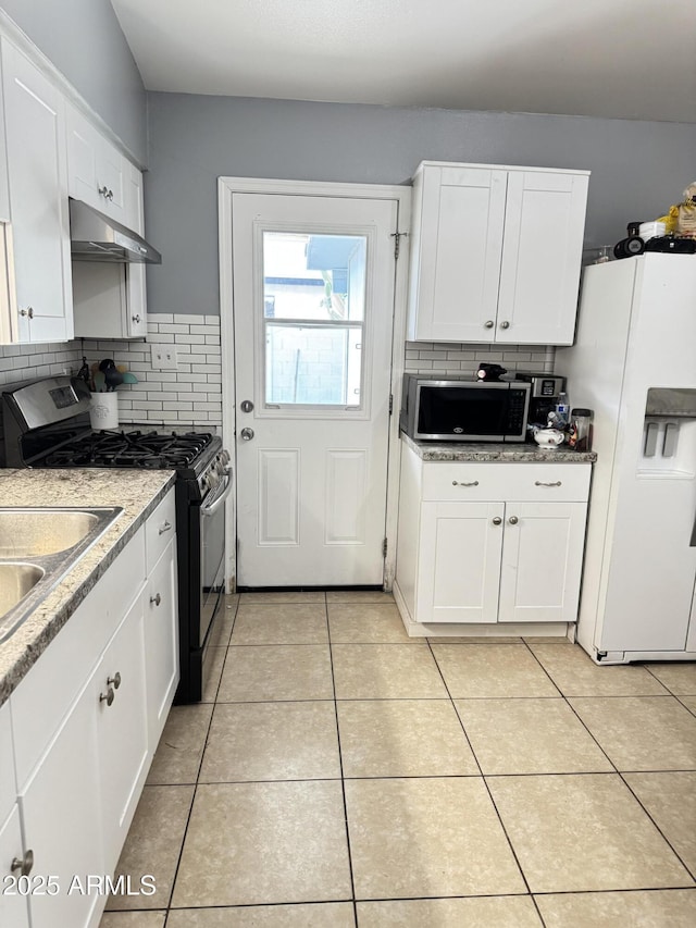 kitchen with under cabinet range hood, stainless steel appliances, decorative backsplash, and light tile patterned floors