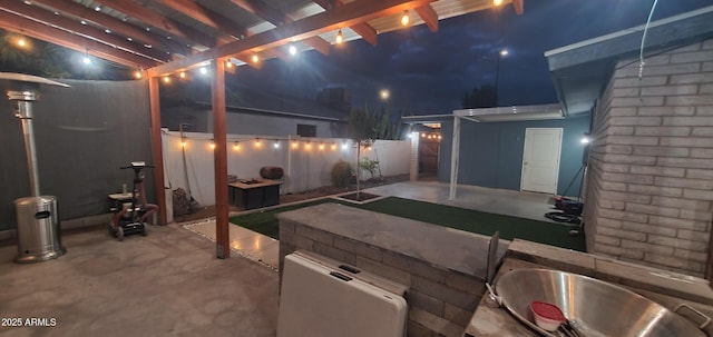 patio at night featuring fence and a pergola