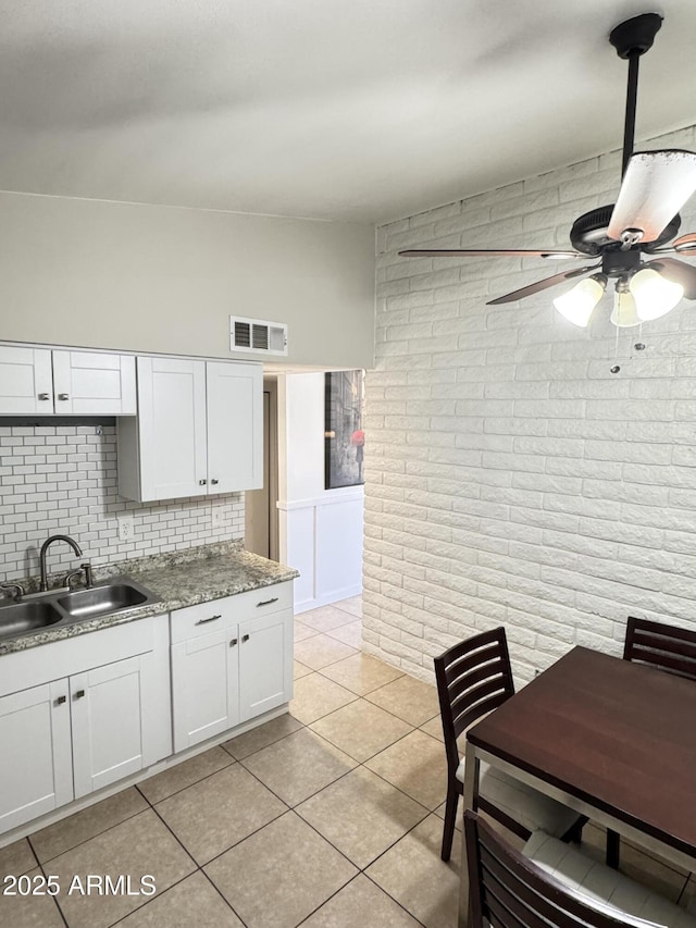 kitchen with visible vents, brick wall, light tile patterned flooring, a sink, and white cabinetry