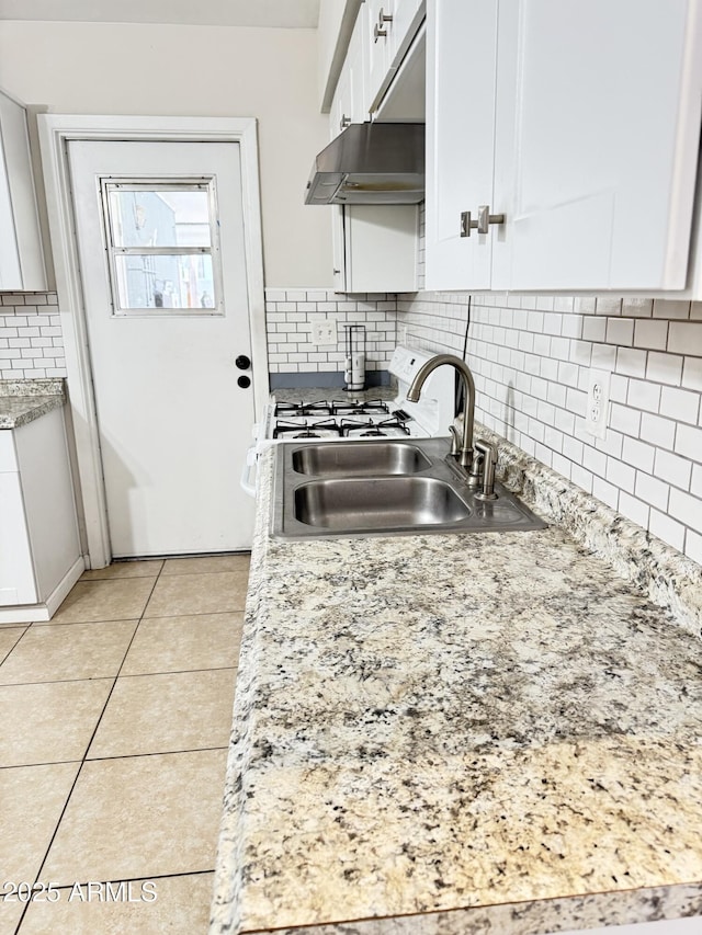 kitchen featuring a sink, under cabinet range hood, tasteful backsplash, light tile patterned flooring, and white cabinets