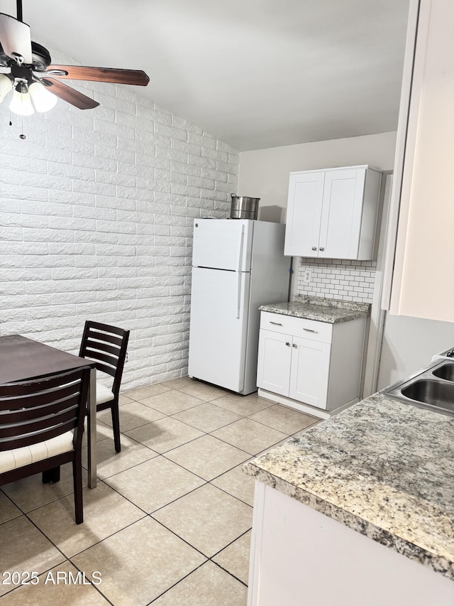 kitchen with a sink, white cabinetry, freestanding refrigerator, brick wall, and light tile patterned floors