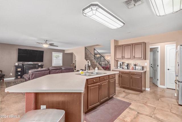 kitchen with ceiling fan, a center island with sink, sink, and stainless steel refrigerator