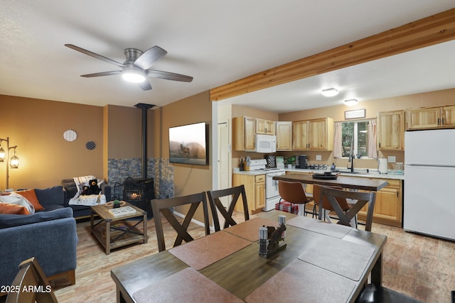 dining room with ceiling fan, a wood stove, sink, and light wood-type flooring