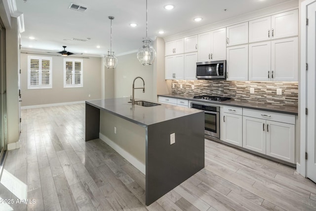 kitchen with appliances with stainless steel finishes, sink, white cabinets, and a center island with sink