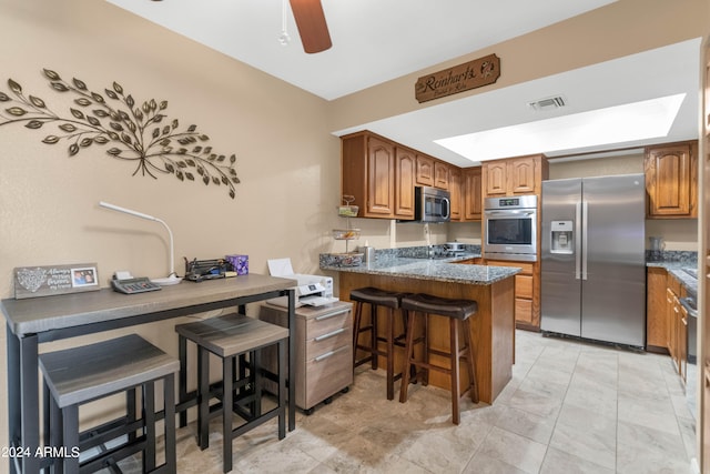 kitchen featuring kitchen peninsula, ceiling fan, a kitchen breakfast bar, dark stone countertops, and stainless steel appliances