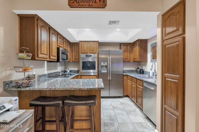 kitchen with stone counters, a tray ceiling, kitchen peninsula, stainless steel appliances, and a breakfast bar area