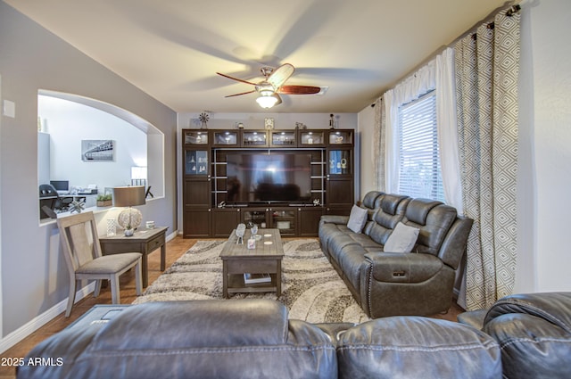 living area featuring a ceiling fan, arched walkways, and baseboards